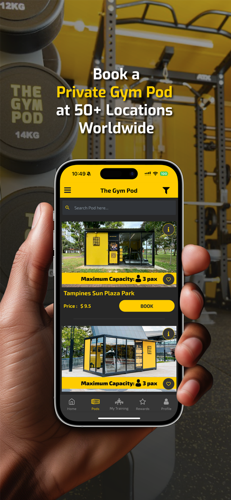 A hand holding a smartphone displaying The Gym Pod app with private gym location options and book buttons.
