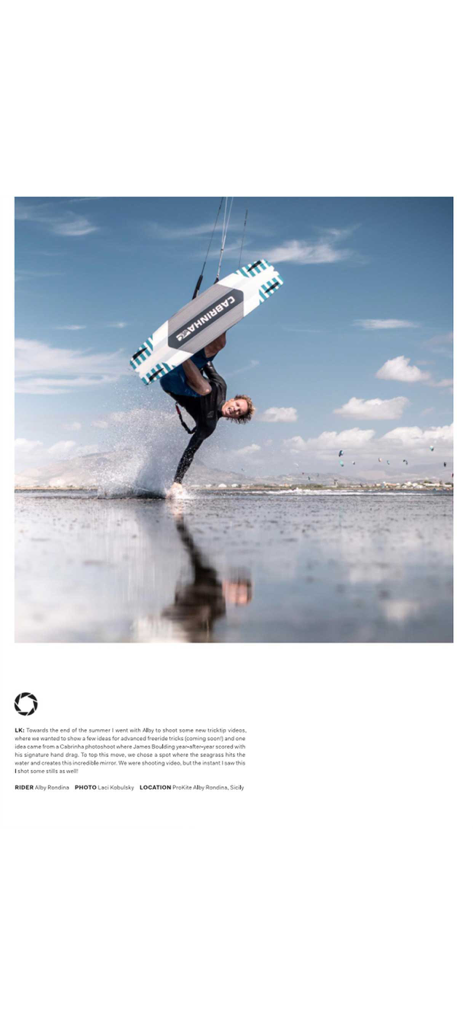 Un kiteboarder profesional realizando un truco de arrastre de manos en aguas poco profundas con un reflejo claro.