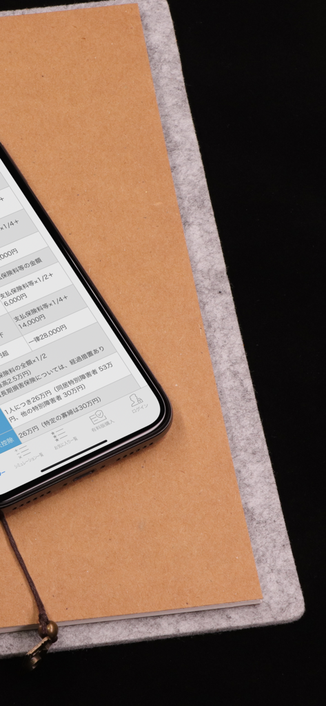FP便利帳 - A smartphone displaying Japanese financial and tax tables from the FP Handbook app resting on a notebook