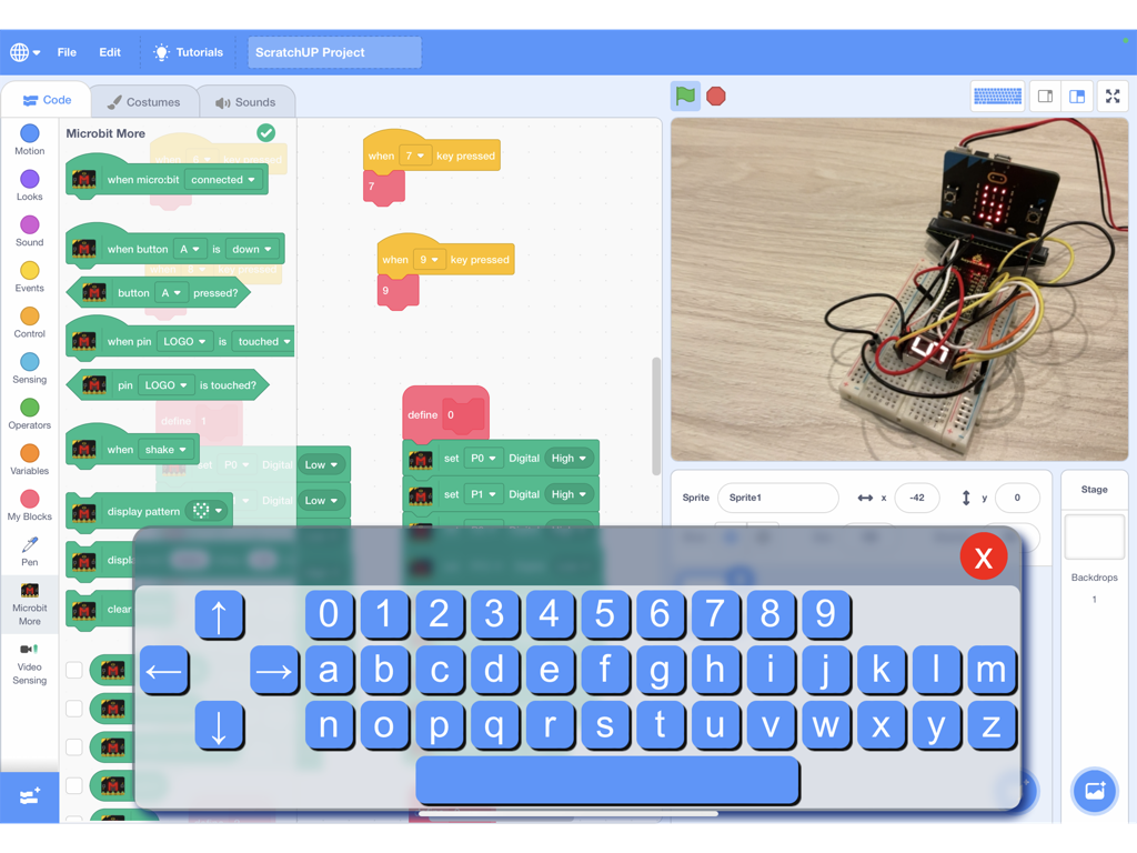 ScratchUP - ScratchUP iPad app interface showing block coding blocks, a virtual keyboard, and a live camera feed of a Microbit hardware project
