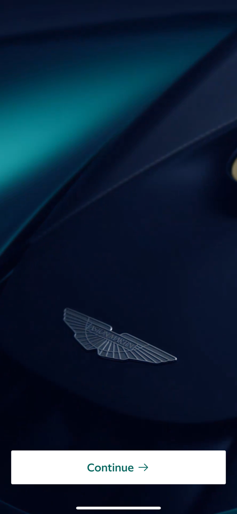The Aston Martin Magazine App - Close-up of the Aston Martin silver winged logo on a dark blue car hood with a continue button