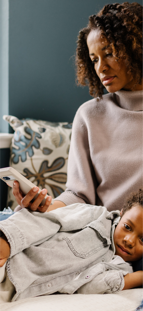 Doctor On Demand - A woman using the Doctor On Demand app on her phone while her child lies in her lap