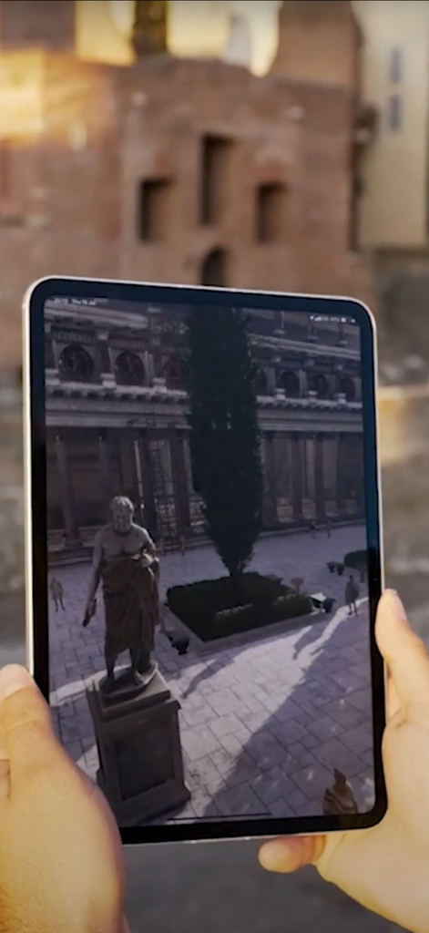 Una persona tiene in mano un tablet che mostra una ricostruzione in realtà aumentata di antiche rovine romane di fronte al sito storico reale