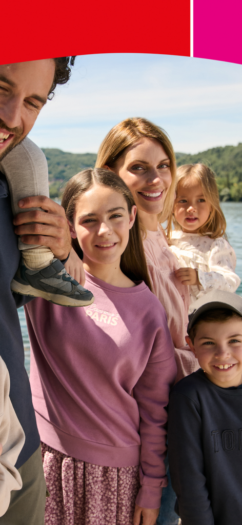 Eine glückliche Familie mit drei Kindern lächelt draußen in Freizeitkleidung