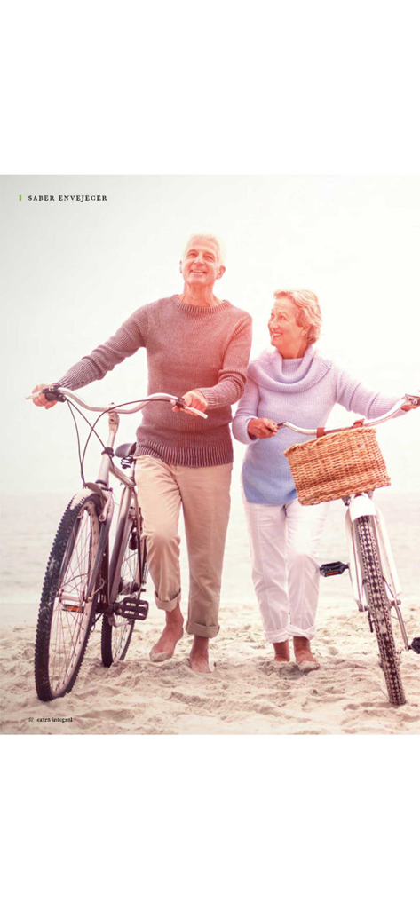 Una pareja de adultos mayores activa caminando con sus bicicletas por una playa arenosa representando el envejecimiento saludable