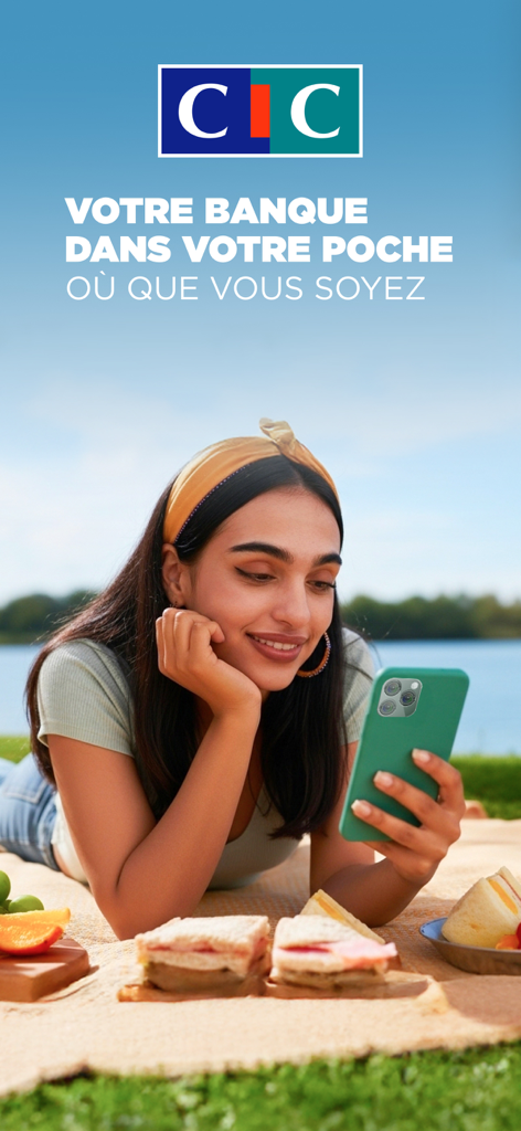 A woman using the CIC bank app on her smartphone during a picnic.