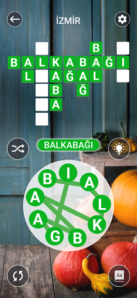Kelime Gezmece - A crossword puzzle level in the Kelime Gezmece mobile game featuring a word search wheel and a rustic pumpkin themed background