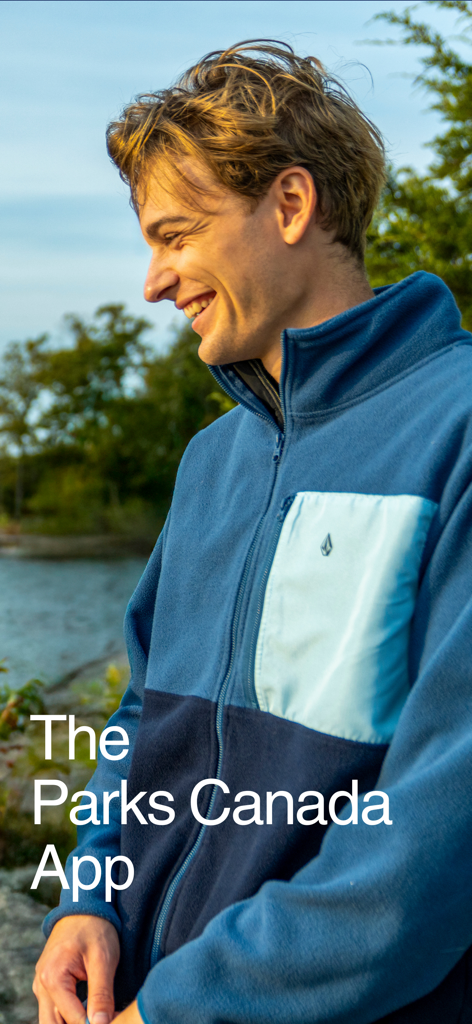 Un uomo sorridente che indossa una giacca in pile blu all'aperto con il testo L'App Parchi del Canada