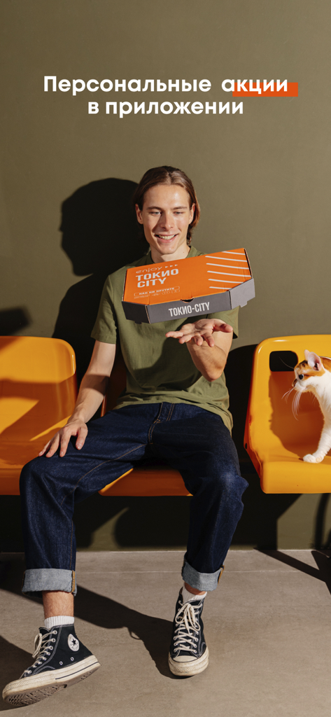 ТОКИО-CITY — заказ еды онлайн - Un hombre joven lanzando una caja de entrega de comida de Tokyo City mientras está sentado junto a un gato blanco