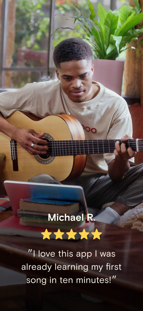 Simply Guitar - Learn Guitar - A young man playing an acoustic guitar while following a lesson on a tablet with a five star review