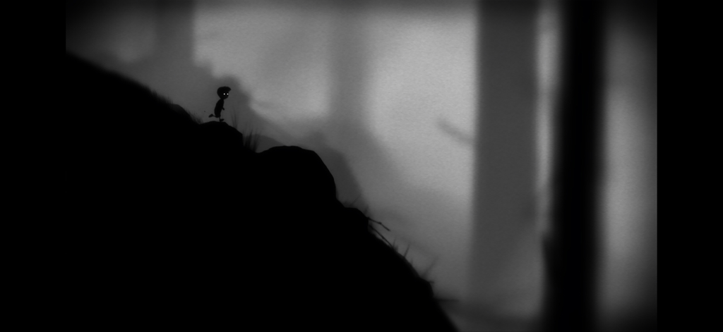 Playdead's LIMBO - Una silueta de un niño de pie en una colina rocosa en un bosque oscuro y brumoso del juego LIMBO de Playdead