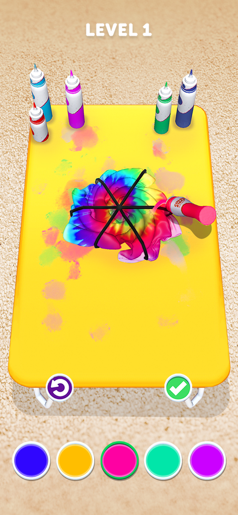 Tie Dye - Pantalla del juego móvil mostrando una tela en espiral siendo teñida de rosa en una mesa amarilla.