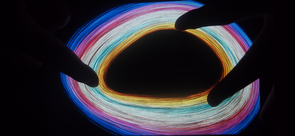 Una persona usa il multi-touch per creare un vibrante vortice circolare di particelle luminose colorate nell'app Atomus.