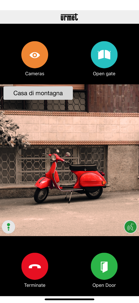 Urmet CallMe - Pantalla de la app Urmet CallMe mostrando una transmisión de vídeo en directo con controles de cancela y puerta