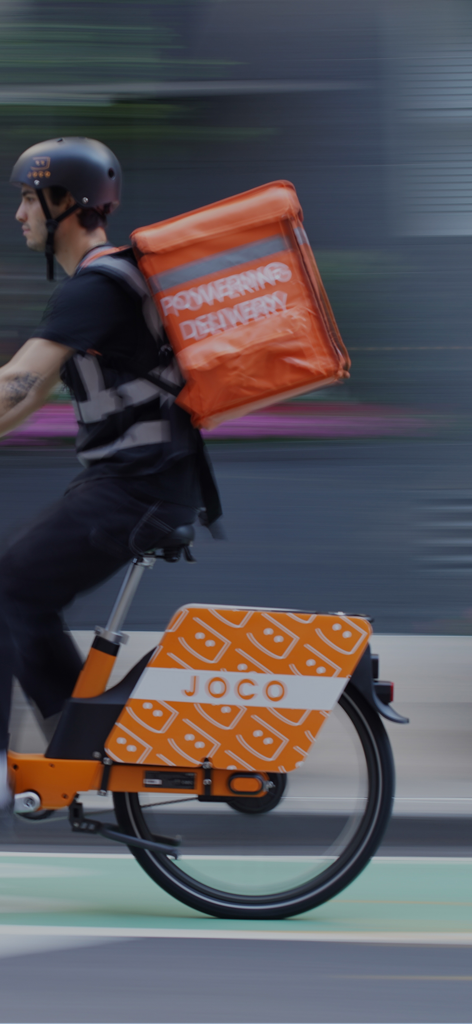 A courier riding a JOCO e-bike with a large orange delivery backpack in motion