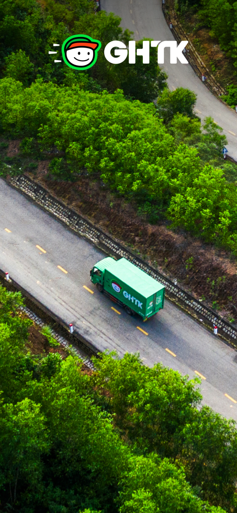 A green GHTK delivery truck driving on a winding road through lush greenery in Vietnam