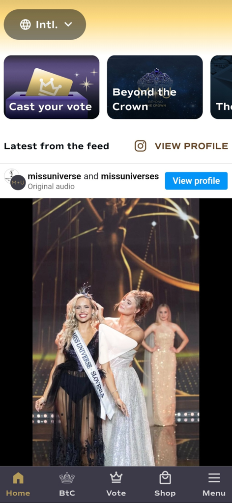 Home screen of the Miss Universe app showing a social feed video of Miss Universe Slovenia and navigation buttons for voting and the shop.
