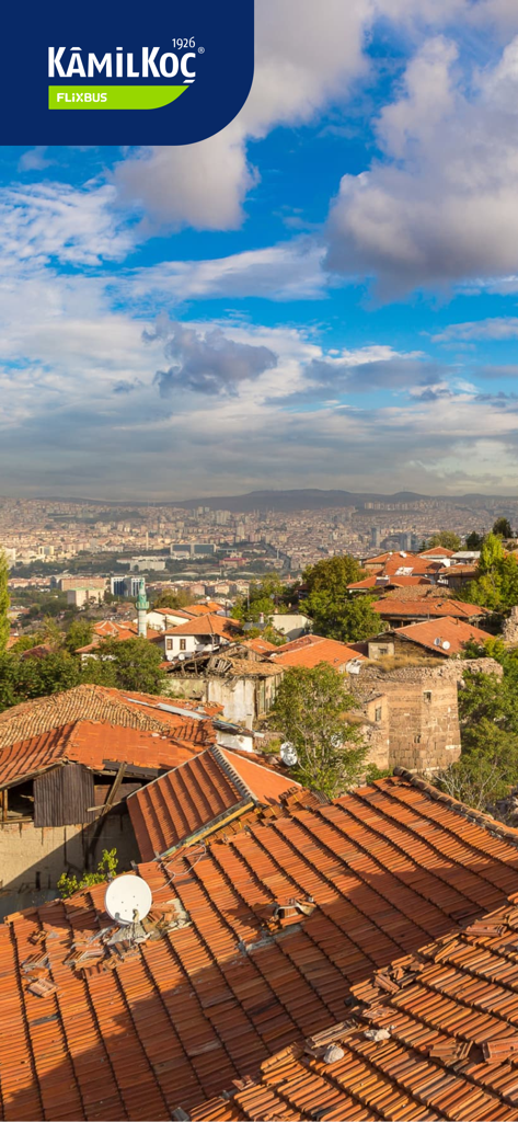 A scenic aerial view of a Turkish city with traditional orange tile roofs under a blue sky featuring the Kamil Koc logo