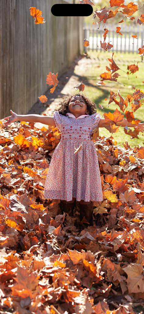 Sound Touch - Seasons (School) - A young girl smiling with her arms open while playing in a large pile of fallen brown autumn leaves