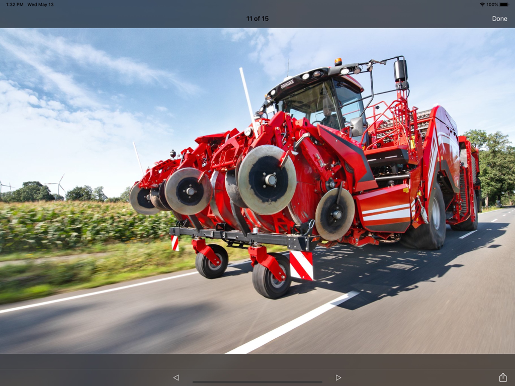 GRIMME - A large red GRIMME harvester machine traveling on a paved road under a bright sky