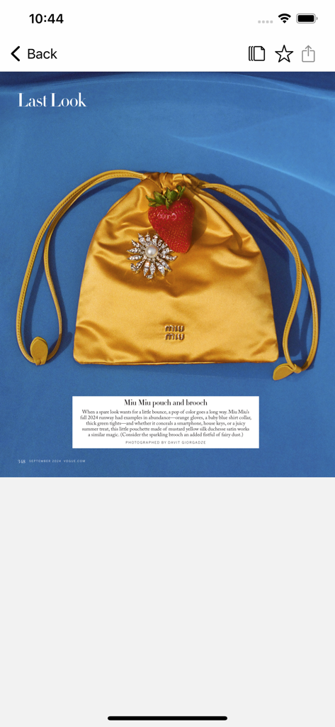 Une pochette en satin Miu Miu jaune et une broche en cristal avec une fraise sur fond bleu, telle que vue dans l'application Vogue.
