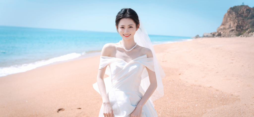 Una mujer con un vestido de novia blanco sonriendo en una playa soleada.