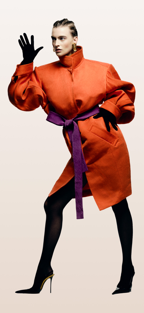 Grazia: Fashion, Beauty & News - Fashion model posing in an orange designer coat with purple sash