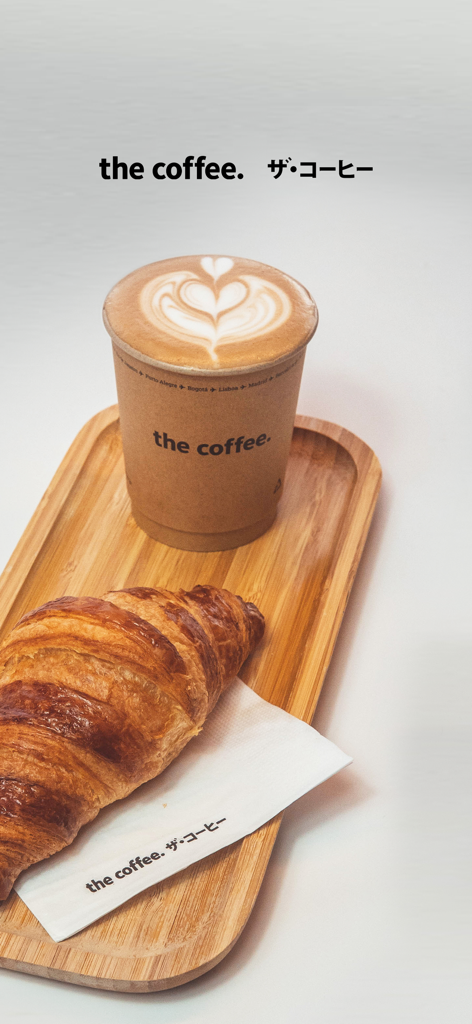 The Coffee - A minimalist paper cup of latte with heart-shaped art and a croissant on a wooden tray