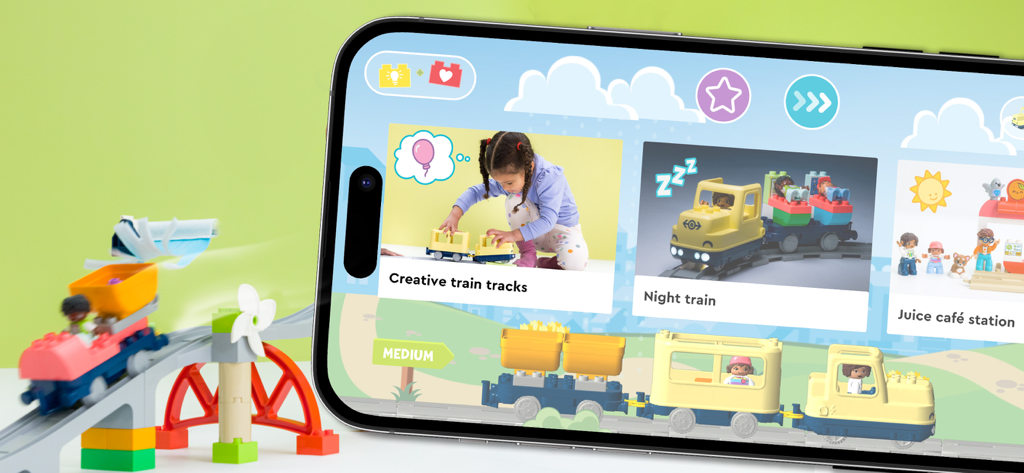 Un smartphone mostrando la aplicación LEGO DUPLO Trenes junto a un tren de juguete físico sobre un puente