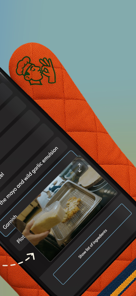 FoodFix app displaying a video recipe tutorial for a garlic emulsion on a smartphone screen resting on an orange oven mitt.